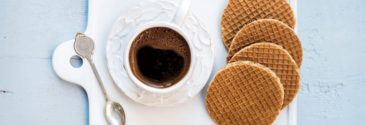 Dutch caramel stroopwafels and cup of black coffee Dutch caramel stroopwafels and cup of black coffee on white ceramic serving board over light blue wooden backdrop, top view